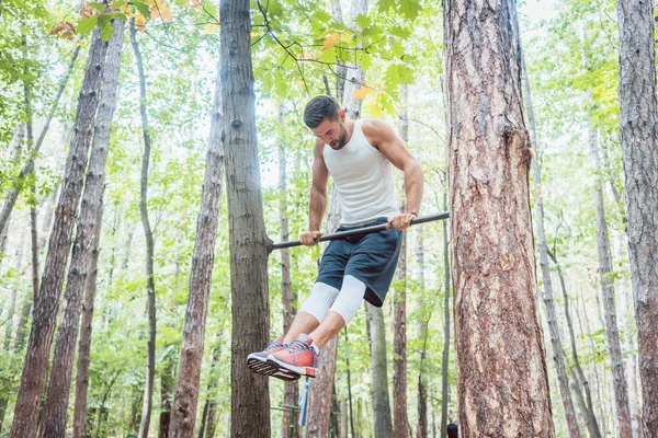 Мужчина занимается гимнастикой в высоком баре в лесу — стоковое фото