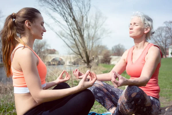 Yaşlı ve genç kadının günlük nehrin yanında Yoga yapması