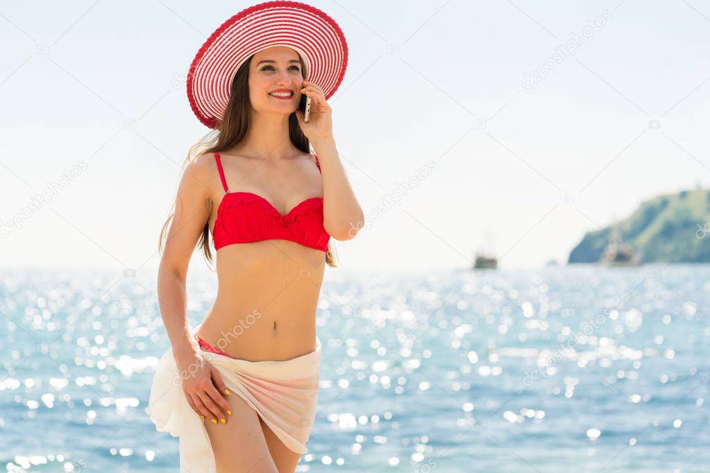 Fashionable fit young woman talking on mobile phone on the beach