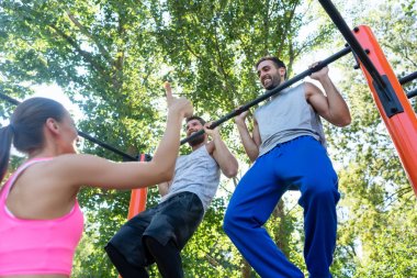 İki güçlü genç adamın pull-up egzersiz, bir sokak egzersiz parkta üst vücut yordamında yaz boyunca onların arkadaşı tarafından motive yinelenen düşük açılı görünüş
