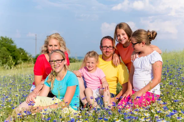 Çayırda çiçekler üzerinde oturan aile — Stok fotoğraf