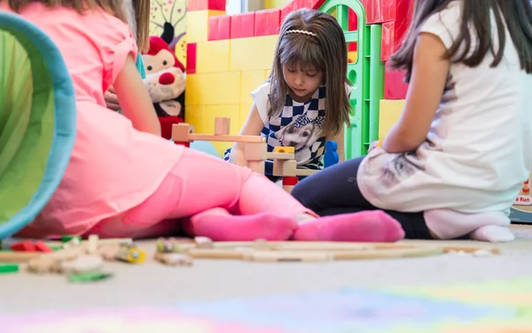 モダンな幼稚園での遊びの中に木製のおもちゃのブロックから構造を構築しながら濃度を見下ろしかわいい幼稚園女の子 — ストック写真