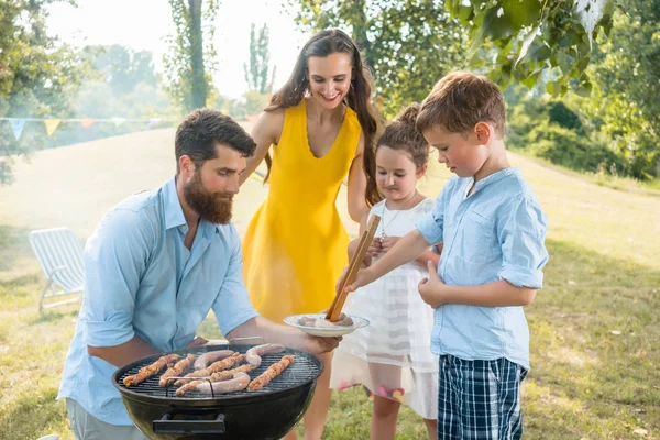 Dedicated father helping son to use wooden tongs during family picnic — Stock Photo, Image
