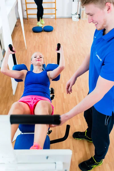 Jovem mulher no ginásio no banco de treino recebendo assistência — Fotografia de Stock