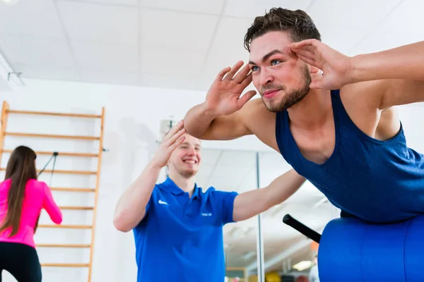 Hombre en el gimnasio en el banco de entrenamiento conseguir ayuda por entrenador personal —  Fotos de Stock