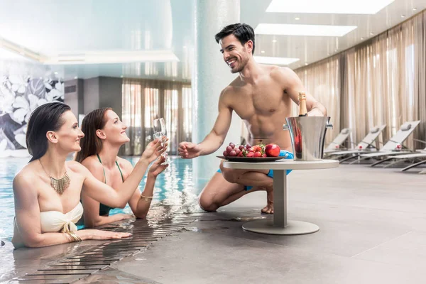 Giovane uomo che serve con champagne due donne in piscina — Foto Stock