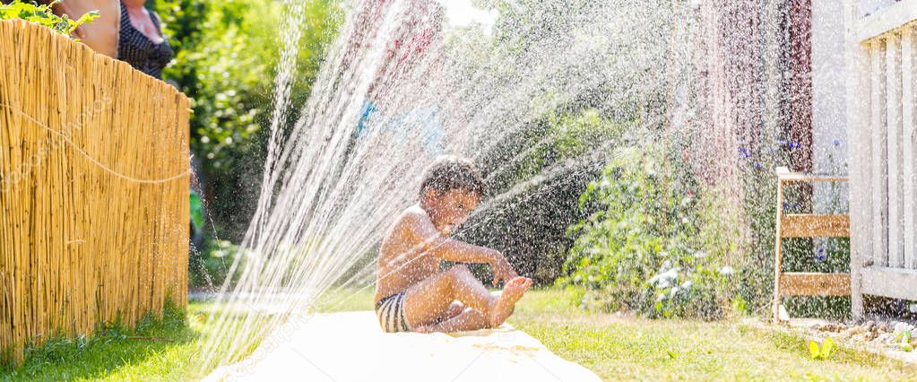 Boy cooling down with garden hose, family in the background