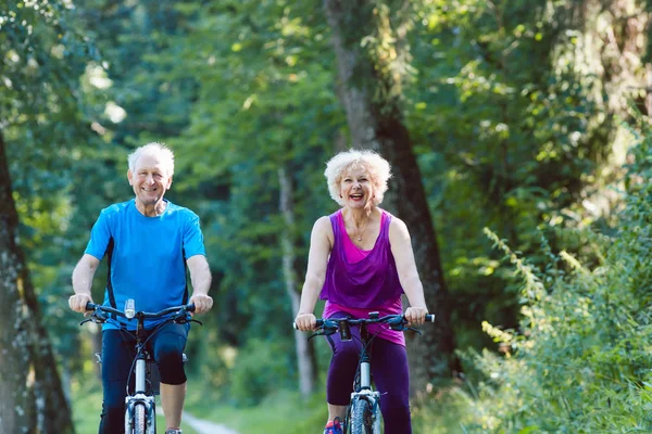 Счастливая и активная пожилая пара катается на велосипедах на открытом воздухе в парке — стоковое фото