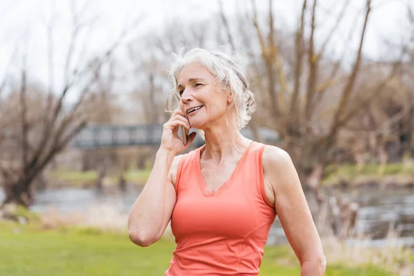 Senior vrouw in de sport kleding ontvangen oproep op haar mobiele telefoon — Stockfoto