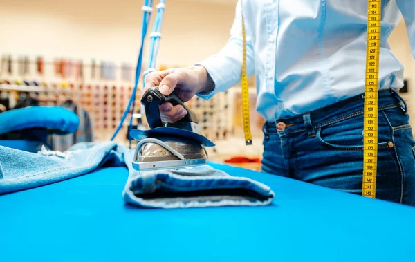 Mitarbeiterin in der Textilreinigung bügelt Hosen — Stockfoto