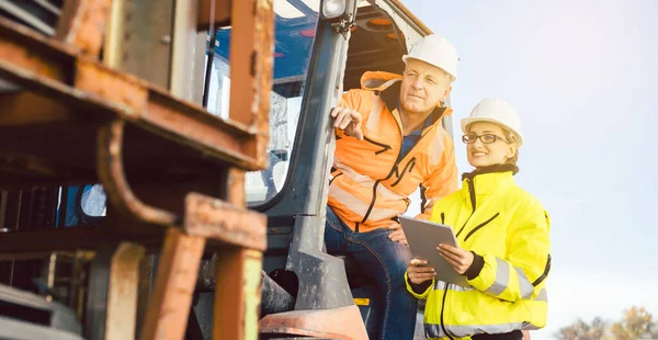 Trabajador en carretilla elevadora y mujeres extranjeras que buscan en la lista de tareas — Foto de Stock