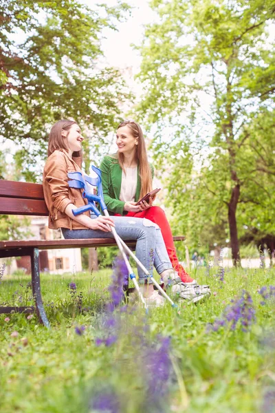 Two women, one healthy and one with a sprained foot, on a bench — Stock Photo, Image