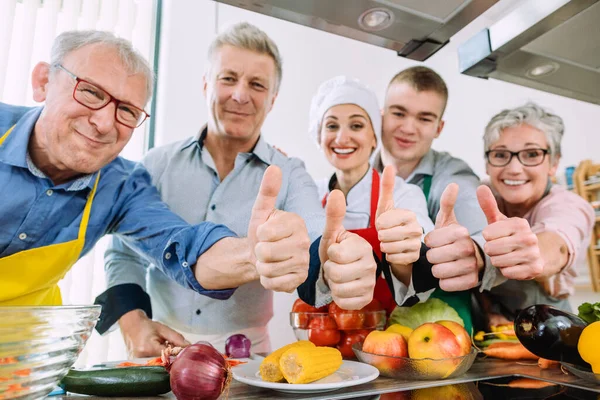 Los alumnos y su nutricionista en una cocina de entrenamiento mostrando pulgares — Foto de Stock