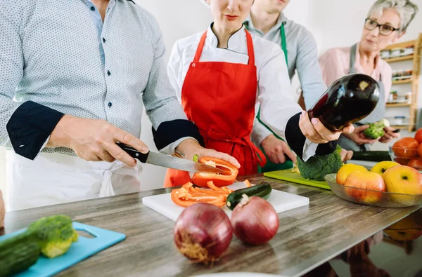 Mann in Trainingsküche schneidet Gemüse unter wachsamen Augen der Ernährungsberaterin — Stockfoto