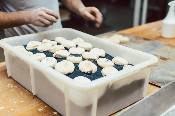 Baker putting poppy seed on raw bread rolls — Stock Photo, Image