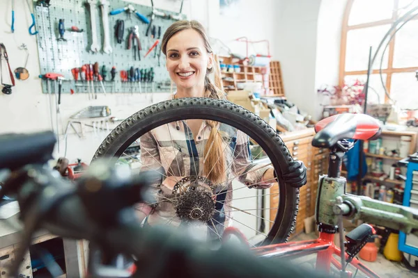 Fiets monteur vrouw kijken door het wiel van de fiets — Stockfoto