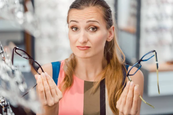 Mulher escolhendo entre dois modelos de óculos no optometrista — Fotografia de Stock