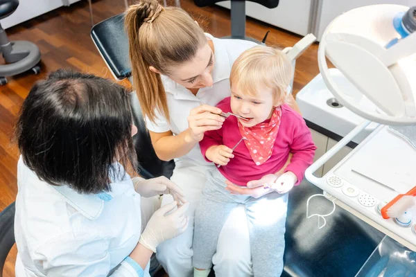 Mujer dentista cuidando dientes de bebé de una niña — Foto de Stock