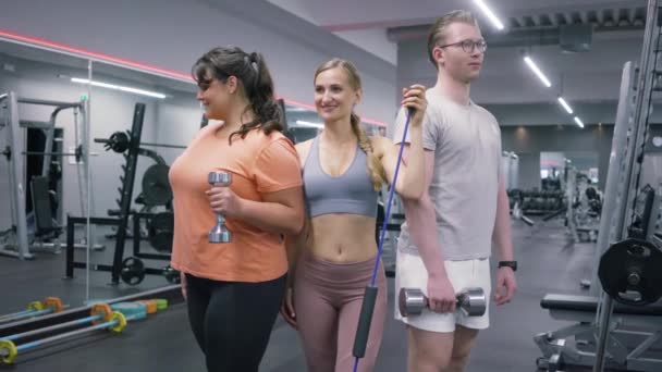 Grupp bestående av två vältränade kvinnor och en man som poserar med hantlar i ett gym — Stockvideo