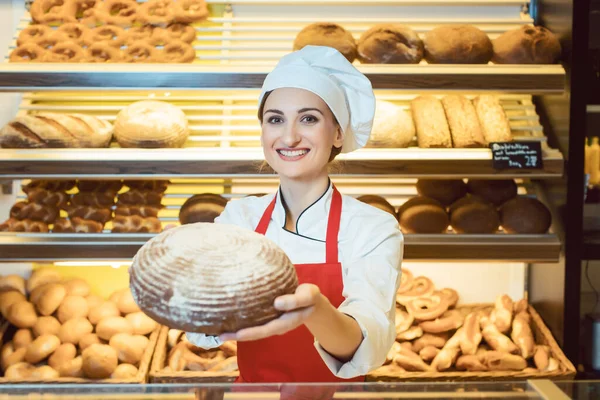 Продавец в фартуке представляет свежий хлеб в булочной — стоковое фото