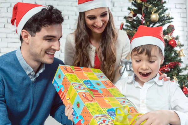 Niño desenvolviendo regalo de Navidad con su familia —  Fotos de Stock