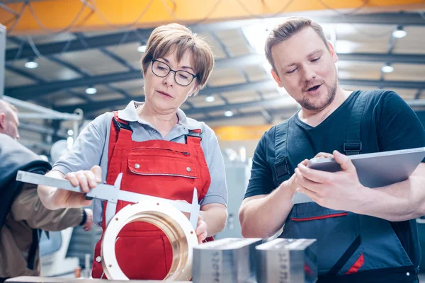 Werknemers die een metalen werkstuk meten — Stockfoto