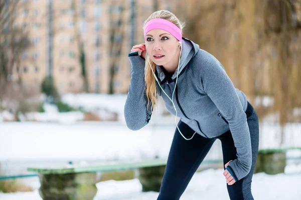 Mujer escuchando música mientras tiene un descanso de correr deporte en invierno —  Fotos de Stock