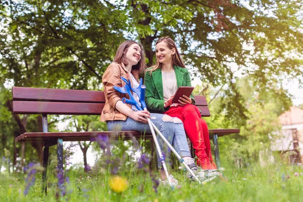 Dos amigos en un parque, uno con los pies rotos y muletas —  Fotos de Stock