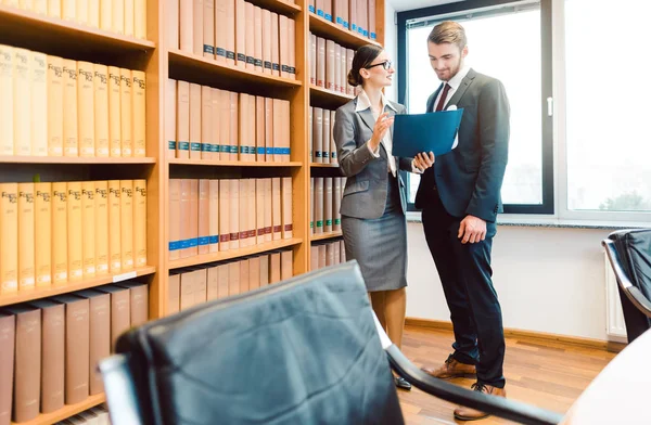 Lawyers in library of law firm discussing strategy in a case holding file — Stock Photo, Image