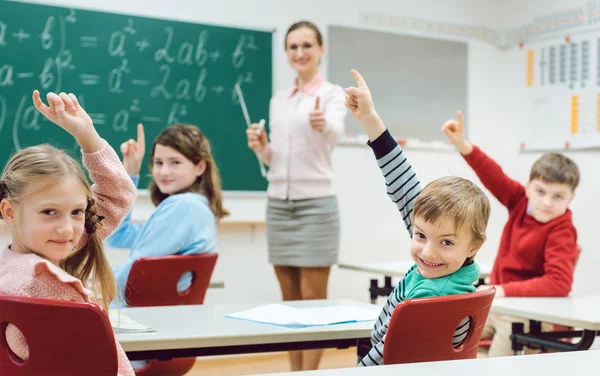 Студенты в классе поднимают руки, чтобы ответить на вопрос — стоковое фото