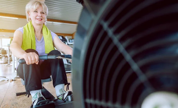 Mulher sênior na máquina de remo em um ginásio de fitness — Fotografia de Stock