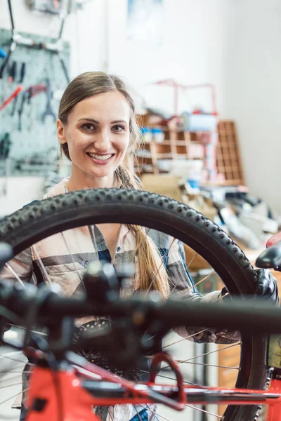 Mujer mecánica de bicicleta mirando a través de la rueda de la bicicleta —  Fotos de Stock