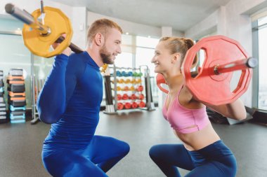 Spor salonunda iki kadın ve bir erkek ağırlıkları yarışıyor.
