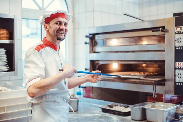 Chef sorrindo colocando pizza no forno em uma cozinha do restaurante — Fotografia de Stock