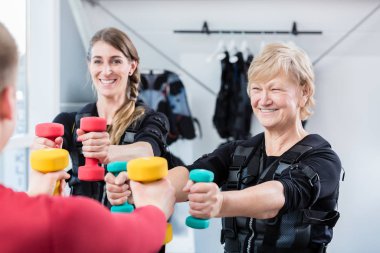 Kablosuz EM spor salonunda dambılları olan yaşlı ve genç bir kadın.
