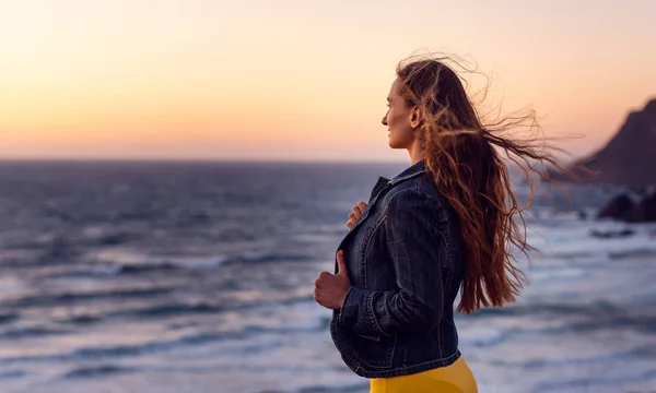Mujer en una playa al atardecer con el viento en su pelo —  Fotos de Stock