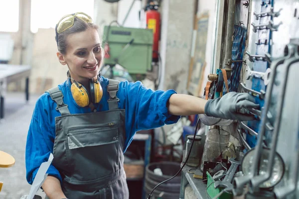 Frau in Fabrik greift Werkzeug von Wandhalterung — Stockfoto