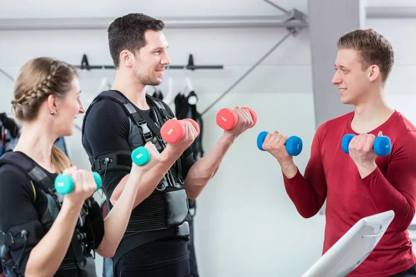 Personal trainer working with couple in ems center to train the biceps — 스톡 사진
