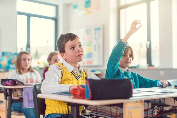 Menino estudante em sala de aula sabendo uma resposta levantando a mão — Fotografia de Stock