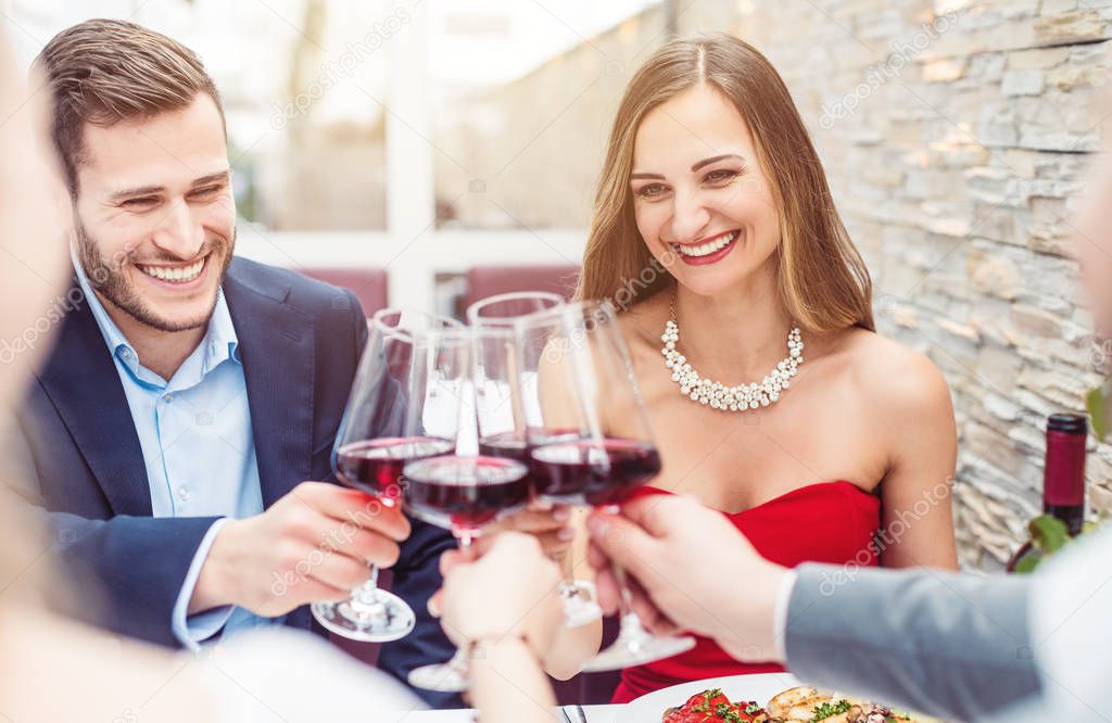 People sitting on restaurant table toasting with red wine