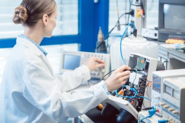 Mühendis kadın test bankında elektronik ürünü ölçüyor.