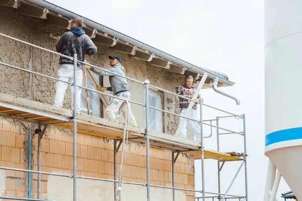 Estucador de pé sobre andaimes no canteiro de obras — Fotografia de Stock