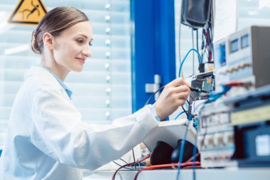 Mühendis kadın test bankında elektronik ürünü ölçüyor.