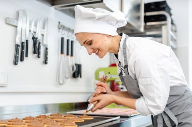 Şekerci kadın kurabiyelerin üstüne krema koymak için pasta torbası kullanıyor.