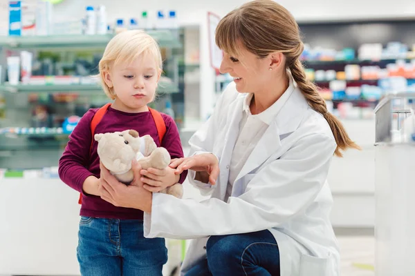 Mujer farmacéutica con cliente infantil y su juguete de peluche — Foto de Stock