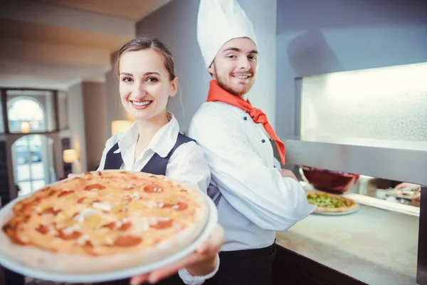 Şef aşçı ve garson restoranda pizza sunuyor. — Stok fotoğraf
