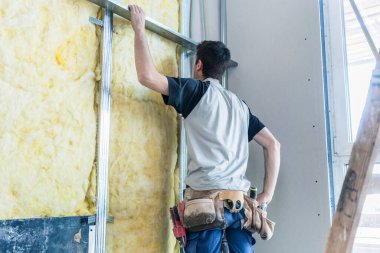 Worker insulating wall of a new building on construction site clipart