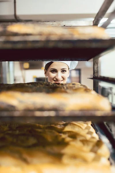 Hermosa panadera mujer mirando a través de pan en hojas — Foto de Stock