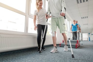 Rehabilitasyondaki insanlar koltuk değnekleriyle yürümeyi öğreniyorlar.