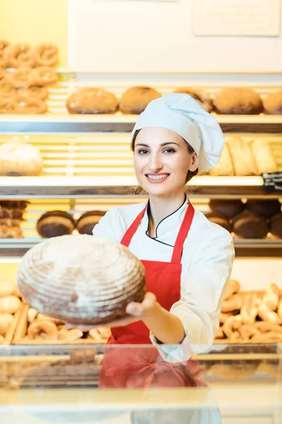Vendedora con delantal presentando pan fresco en una panadería —  Fotos de Stock